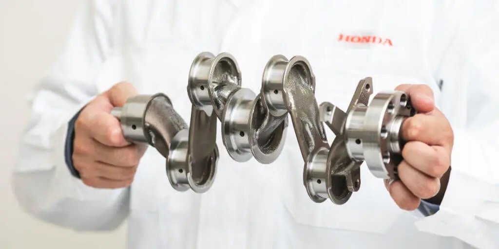 A man holds a crankshaft in his hands