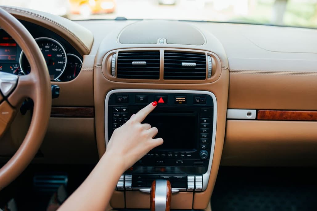 A hand pressing a button on a car's central console with hazard lights on