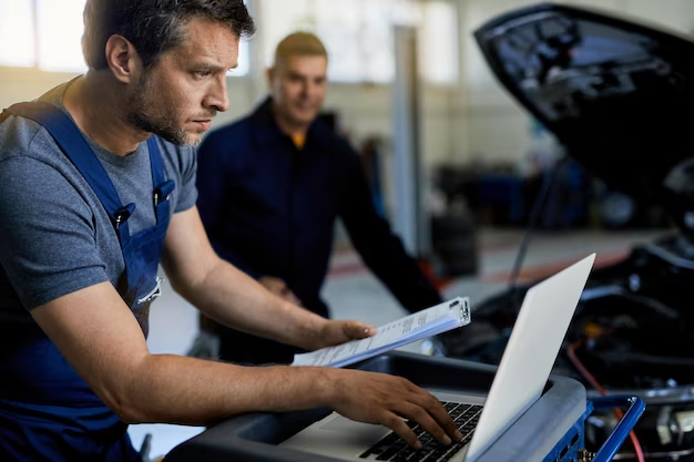 A man works at a computer with papers in his hands near a car