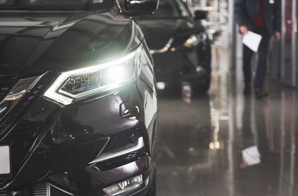 The headlights and the hood of a black luxury car, the black car behind in the car salon